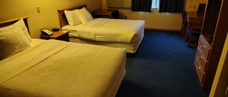 Quarto de hotel com duas camas, uma escrivaninha, cômoda e janela com cortinas.