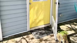A yellow door with a white frame, a small porch with a doormat, and a light fixture on the wall. - Ultimate vacay home, walk to beach, fenced in yard (North Myrtle Beach)