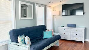 A room with a dark blue sofa, a white dresser, a ceiling fan, and a flat-screen TV mounted on the wall. - Ultimate vacay home, walk to beach, fenced in yard (North Myrtle Beach)