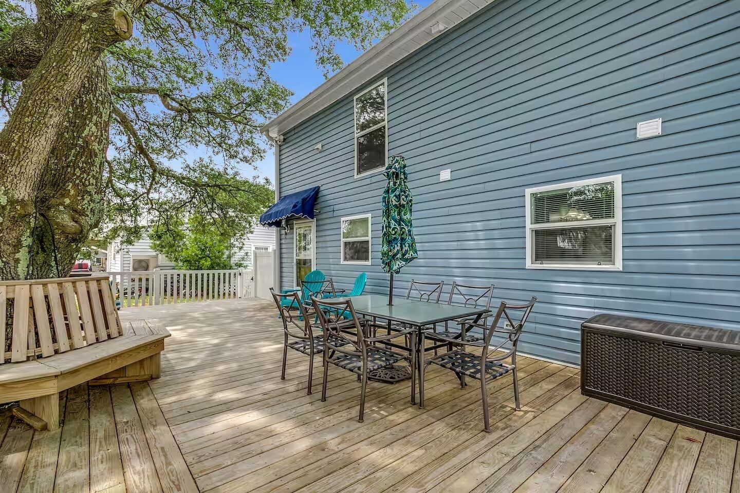 A deck with a table and chairs, a bench, and a covered area with a patterned umbrella.