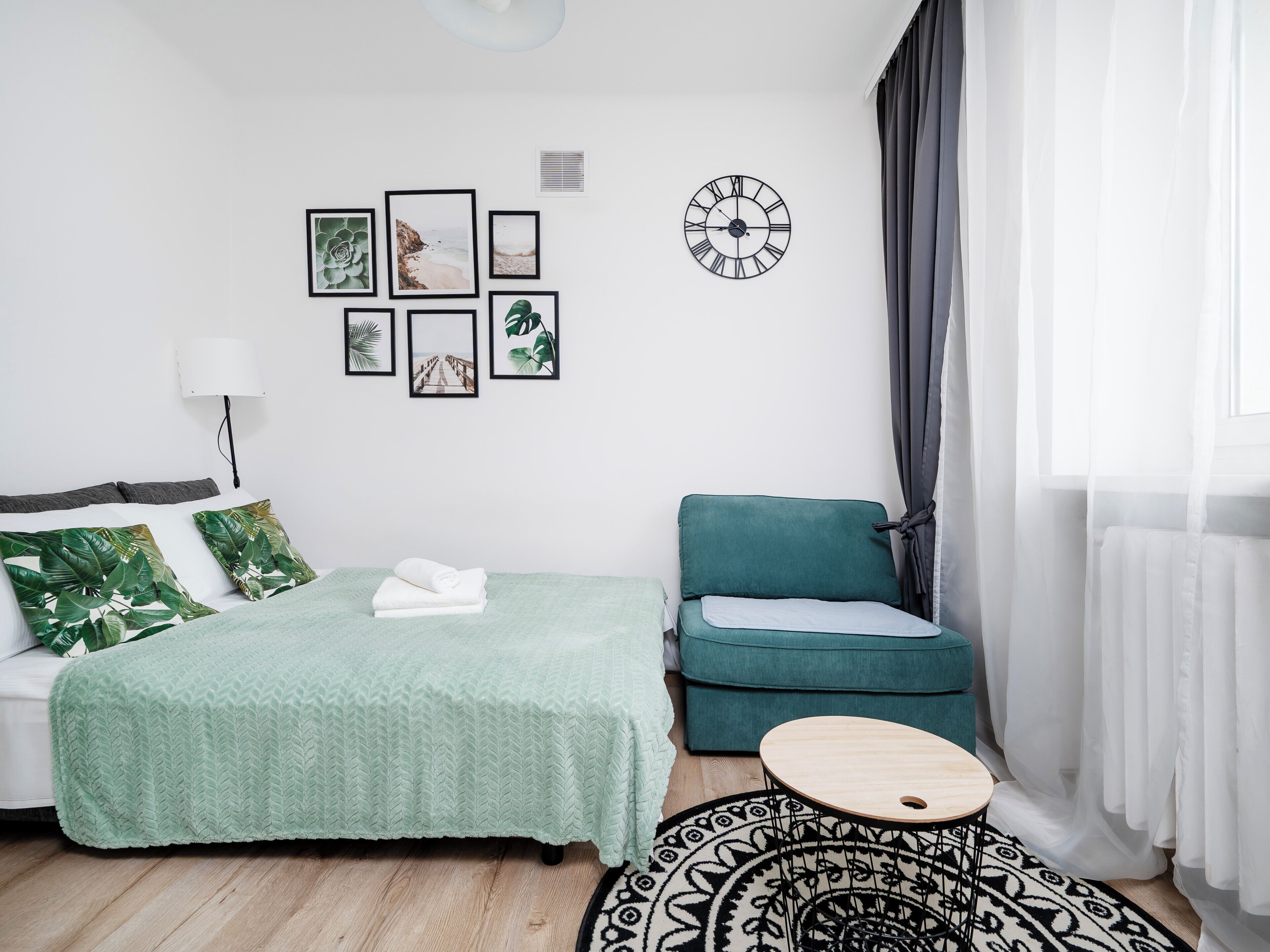 Une chambre à coucher moderne avec un lit, un canapé vert, une table ronde en bois et un tapis à motifs.