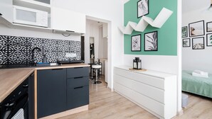 A modern kitchen with a microwave, stove, and black cabinets. There is a dining area with a table and chairs, and a green accent wall with framed pictures.