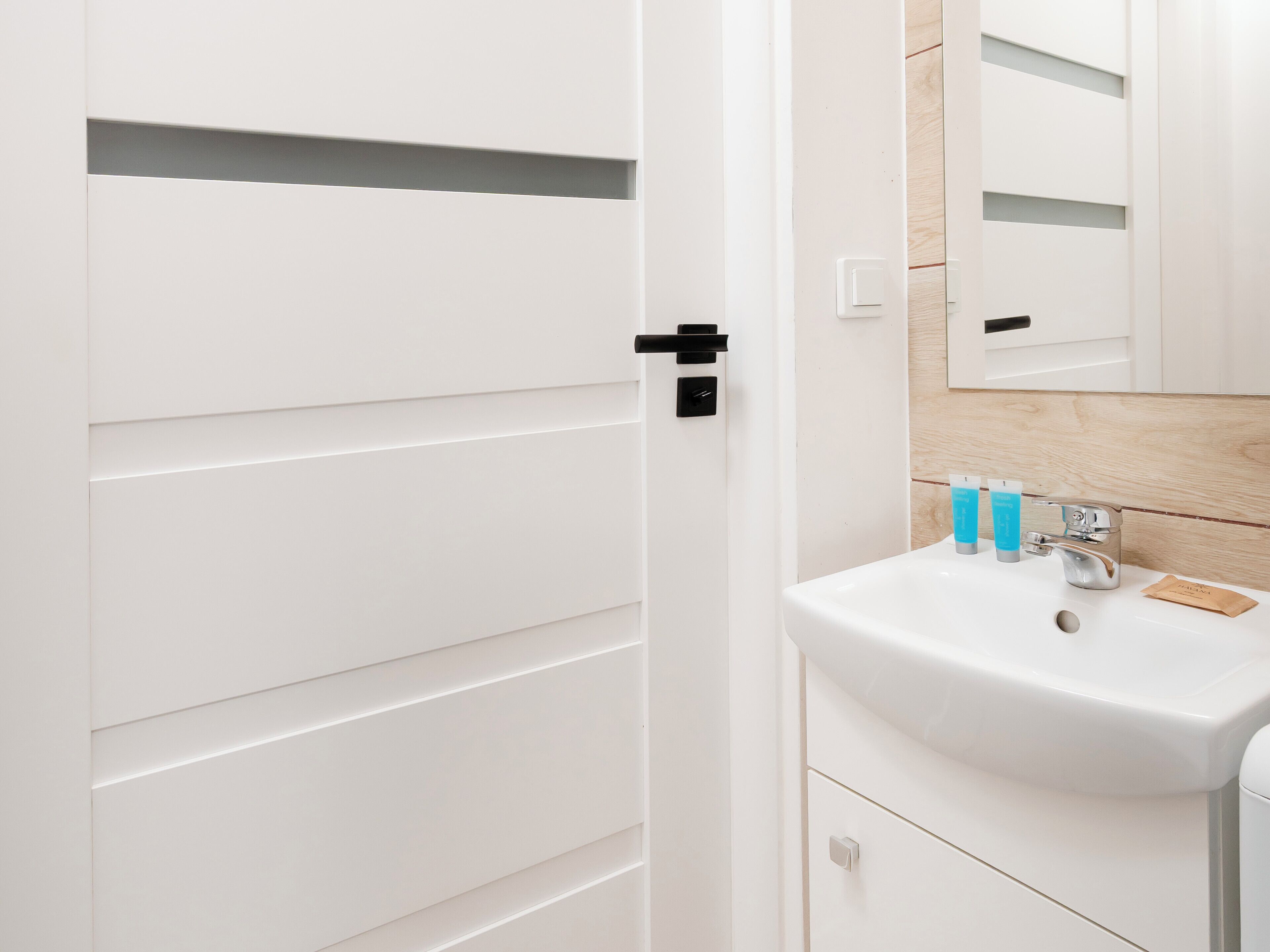 Un bagno moderno con lavandino bianco, specchio e parete rivestita in legno.