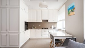 Eine moderne Küche mit weißen Schränken, eine Essecke mit Tisch und Stühlen und ein Gemälde an der Wand.