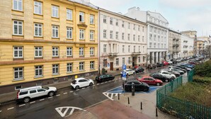 Straßenansicht mit parkenden Autos, einem blauen Parkschild und mehrstöckigen Gebäuden mit Fenstern.