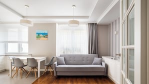 Ein modernes Wohnzimmer mit grauem Sofa, Holzboden und einem Essbereich mit weißem Tisch und Stühlen.