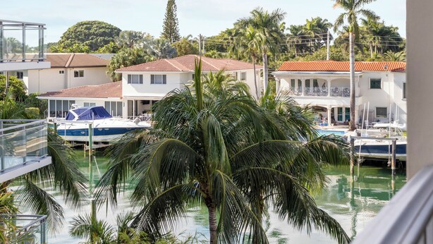 A view of a marina with boats docked, palm trees, and buildings with red-tiled roofs. - Bay Harbor Sunset Apt 4B (Bay Harbor Islands)