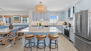 Une cuisine moderne dotée d’un grand îlot central, de tabourets de bar, d’appareils électroménagers en acier inoxydable et de meubles de couleur bleu clair.