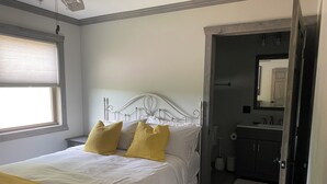 Un dormitorio con cama, ventana y baño visible a través de una puerta abierta.
