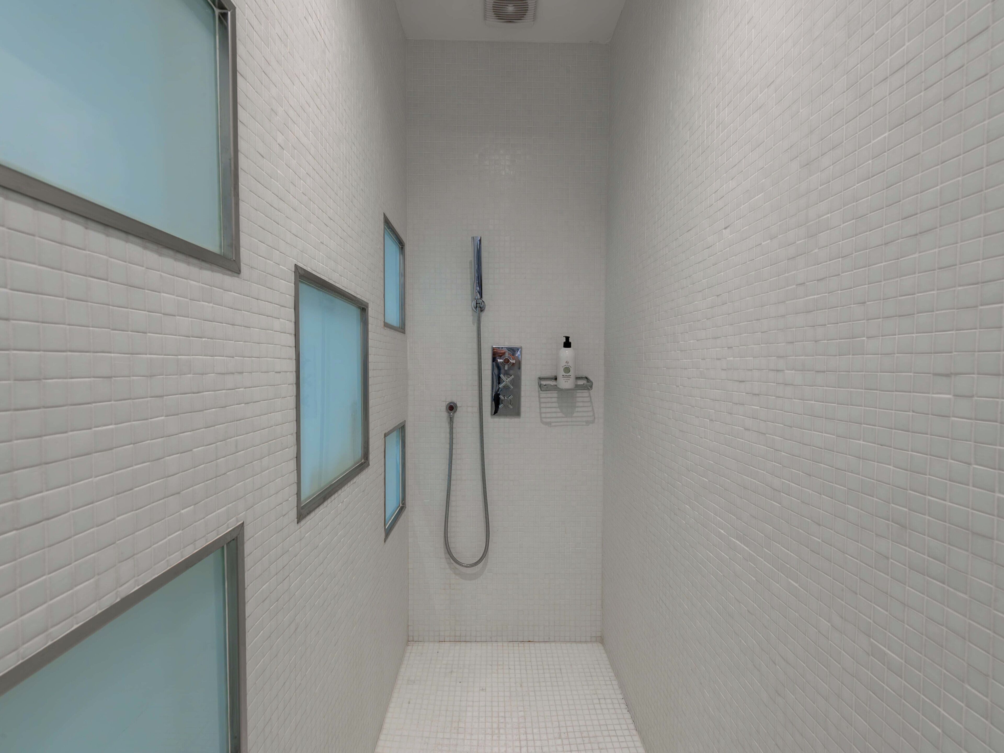 A narrow, tiled shower area with a handheld showerhead and a wall-mounted faucet.