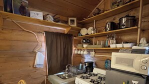 Une cuisine compacte aux murs en bois, équipée d’une cuisinière, d’un réfrigérateur et d’étagères remplies d’ustensiles de cuisine.