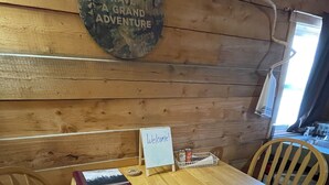 Un intérieur en bois avec une table et des chaises, une pancarte de bienvenue et une autre sur laquelle on peut lire : « VIVONS UNE GRANDE AVENTURE ».