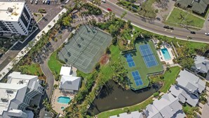 Luchtbeeld van een bezit met een tennisbaan, zwembaden en een aangelegde tuin met palmstruiken.