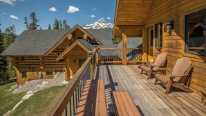 A wooden cabin with a deck, chairs, and a view of a snow-capped mountain. - New! Ski-in/out Log Home beside 104.3 acres with a private hot tub (Big Sky)