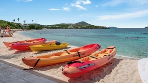 A beach with several kayaks lined up on the sand, a clear blue sky, and a calm sea.