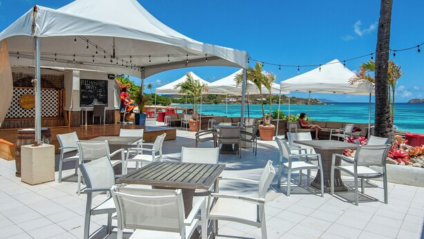 An outdoor patio with white tables and chairs, a bar area, and a view of the ocean.