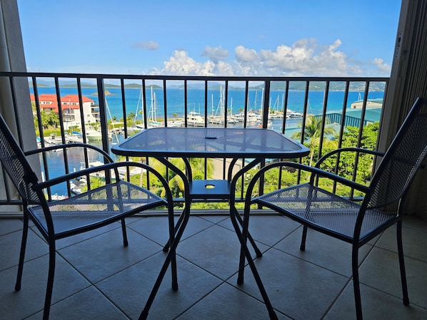 A balcony with a table and two chairs, overlooking a marina with boats and a clear blue sky. - Sapphire Skies... Pools, Beach and restaurants (St Thomas)