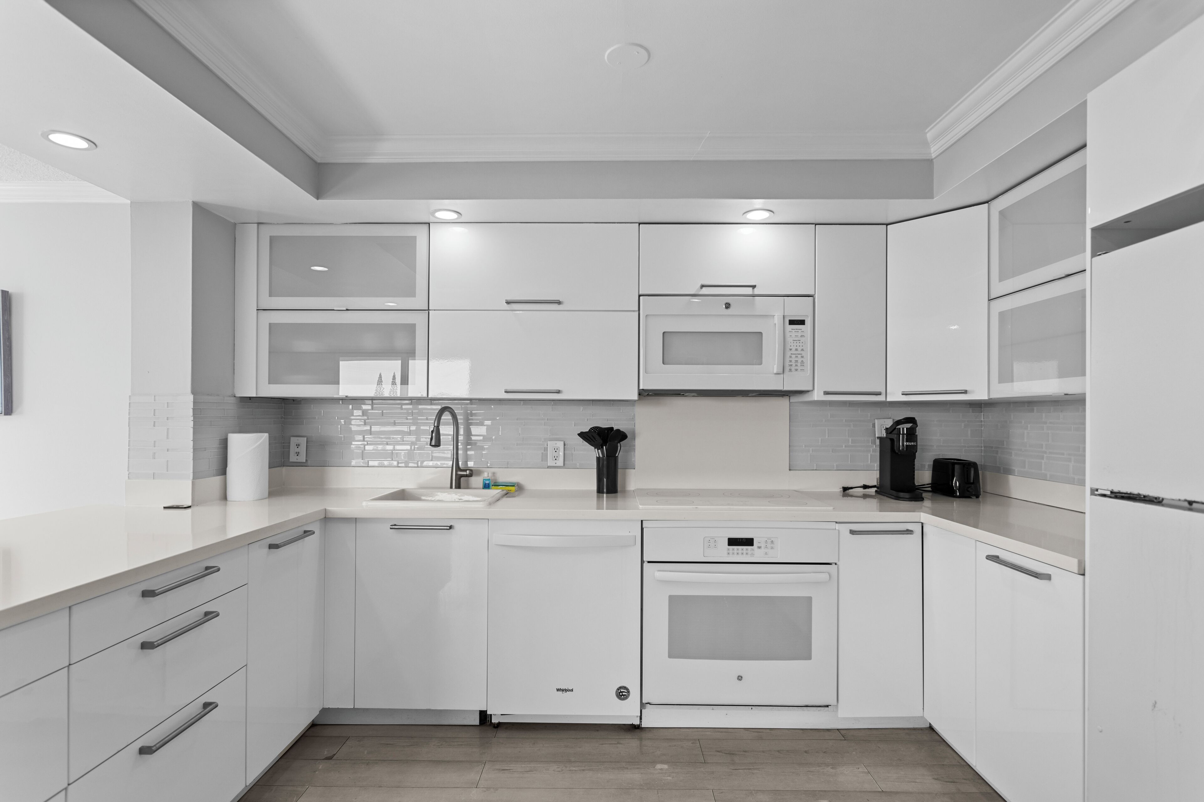A modern kitchen with white cabinetry, a built-in microwave, a dishwasher, and an oven.