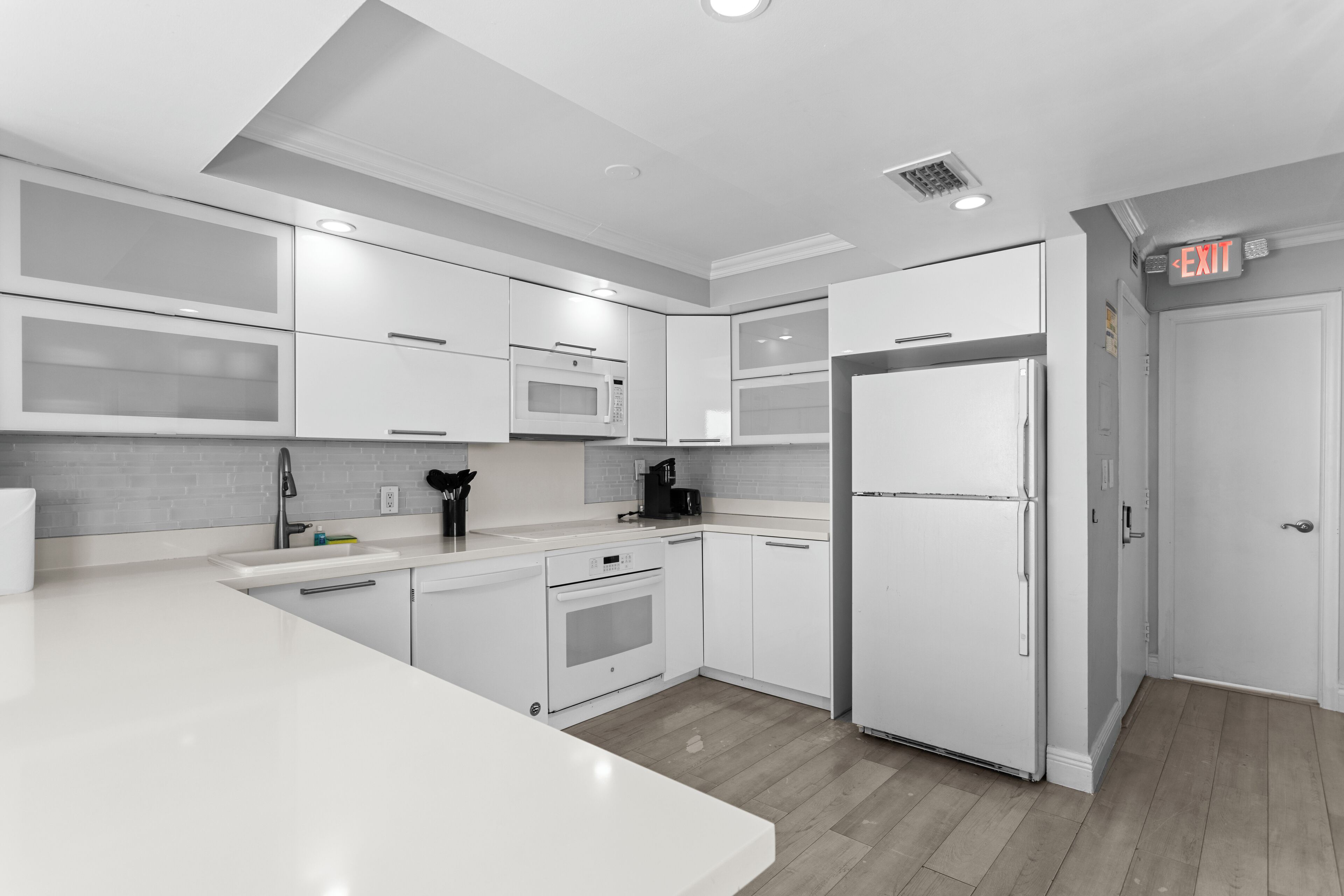 A modern kitchen with white cabinetry, a built-in microwave, a refrigerator, and a coffee maker.