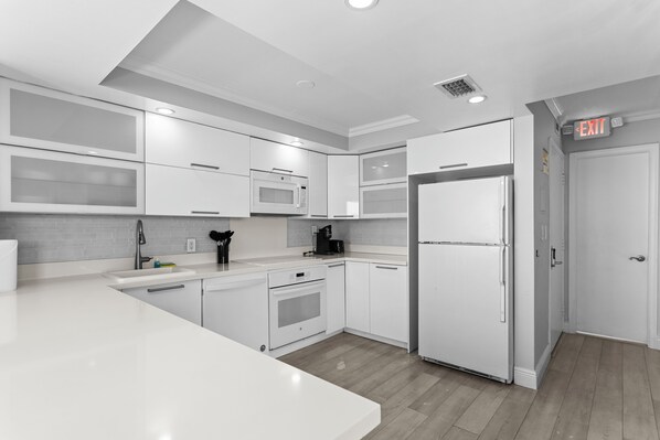 A modern kitchen with white cabinetry, a built-in microwave, a refrigerator, and a coffee maker. - Bay Harbor Sunset Apt 5A (Bay Harbor Islands)