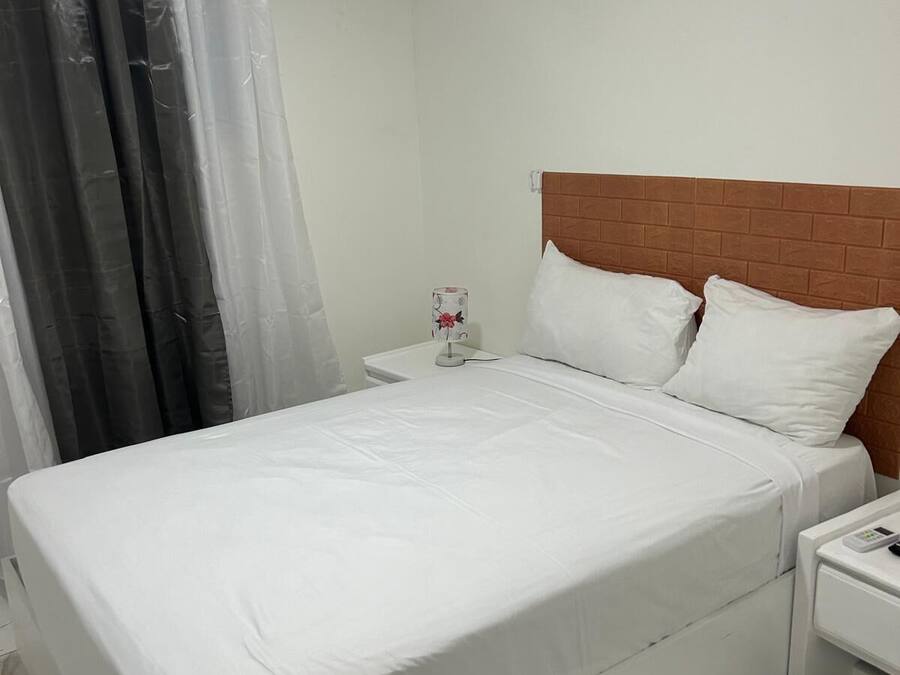 Habitación de hotel con cama, mesita de noche, control remoto y aire acondicionado.