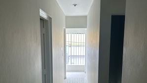 A corridor with a tiled floor leading to a balcony with a metal railing.