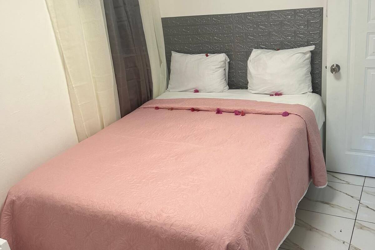 Una cama bien hecha con una colcha rosa, un cabecero gris y almohadas blancas.