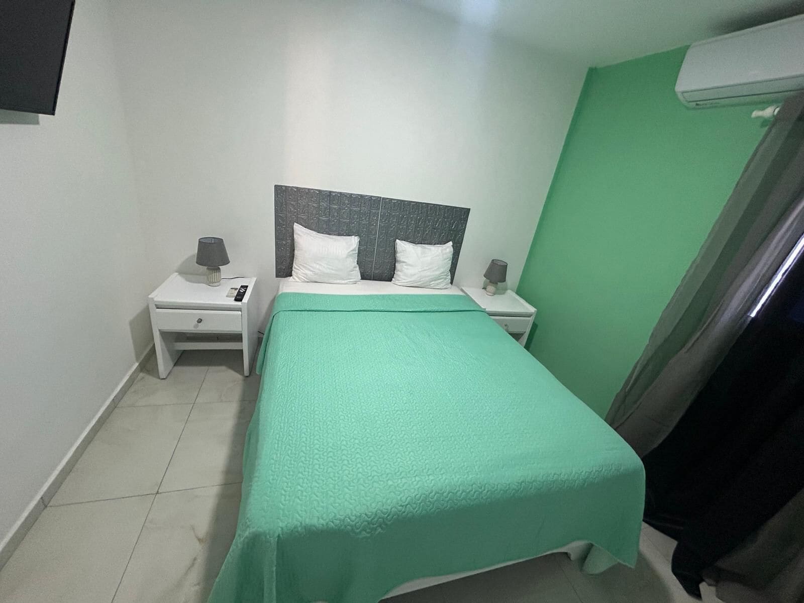 Una camera da letto piccola e ordinata, con un letto, due comodini e un condizionatore d'aria.