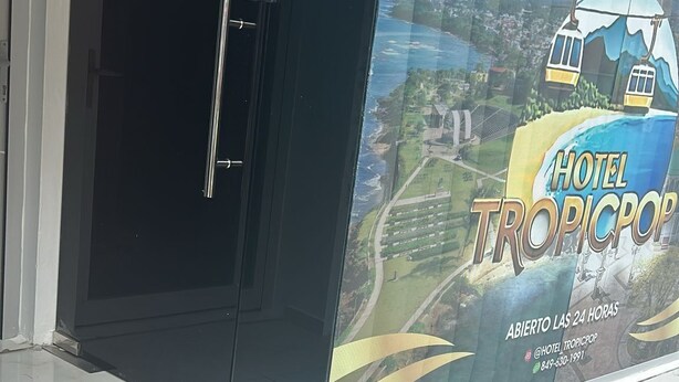 A hotel entrance with a glass door, a tiled floor, and a large advertisement for 'HOTEL TROPICPOP' featuring a tropical theme.