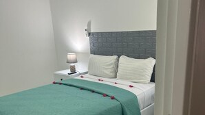 A bedroom with a bed, a nightstand, a lamp, and a wall-mounted thermostat.