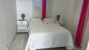 Un dormitorio ordenado con una cama grande, dos mesitas de noche con lámparas y una ventana con cortinas traslúcidas.