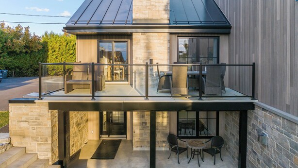 Une maison moderne dotée d’un balcon, d’un espace salon extérieur et d’une façade en pierre.