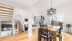 Un vaste espace de vie agrémenté d’un escalier en bois, d’une table à manger avec des chaises et d’une grande fenêtre offrant une vue sur l’extérieur.