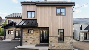 Une maison à deux étages avec une façade en pierre, des fenêtres à encadrement noir et un toit noir.