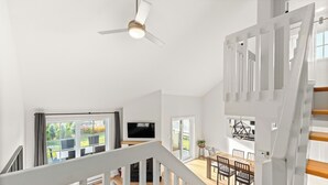 Un vaste espace de vie comprenant un grand téléviseur, une table à manger et un escalier menant à l’étage supérieur.