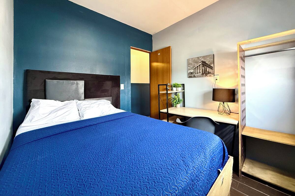 Ein Hotelzimmer mit Bett, Schreibtisch, Stuhl, Spiegel und einer kleinen Pflanze.
