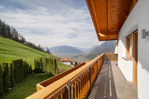 A balcony with a wooden railing overlooking a green hillside and mountains.
