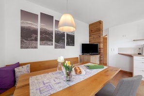 A modern living room with a wooden dining table, a sofa, a TV, and a kitchen area.