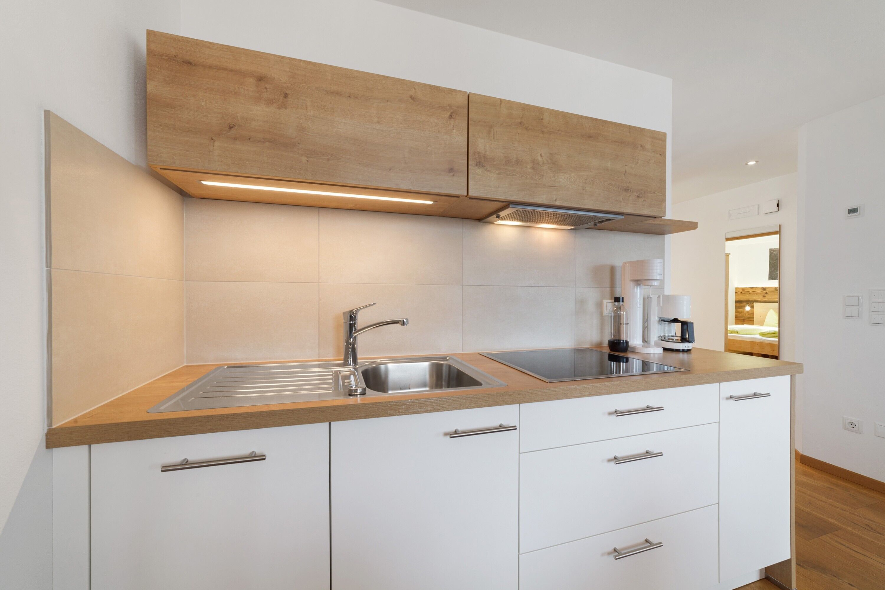 Une cuisine moderne dotée d’un plan de travail en bois, d’un évier en acier inoxydable et de meubles blancs.