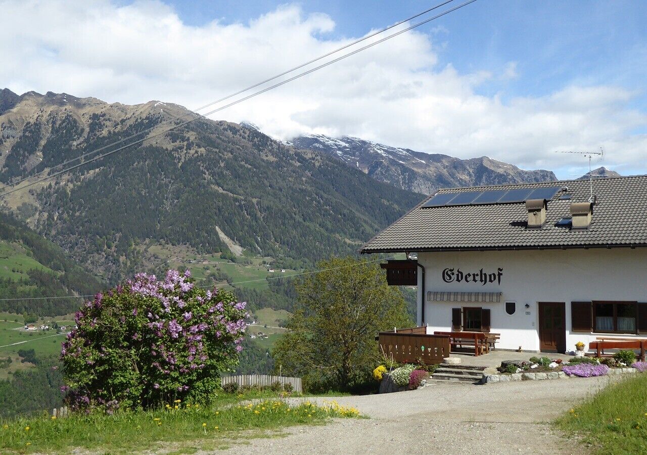 A white building with a sign 'Ederhof' in front of a mountainous landscape.