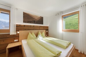 Een kamer met een bed, een houten hoofdeinde, een schilderij en een raam met uitzicht op bergen.