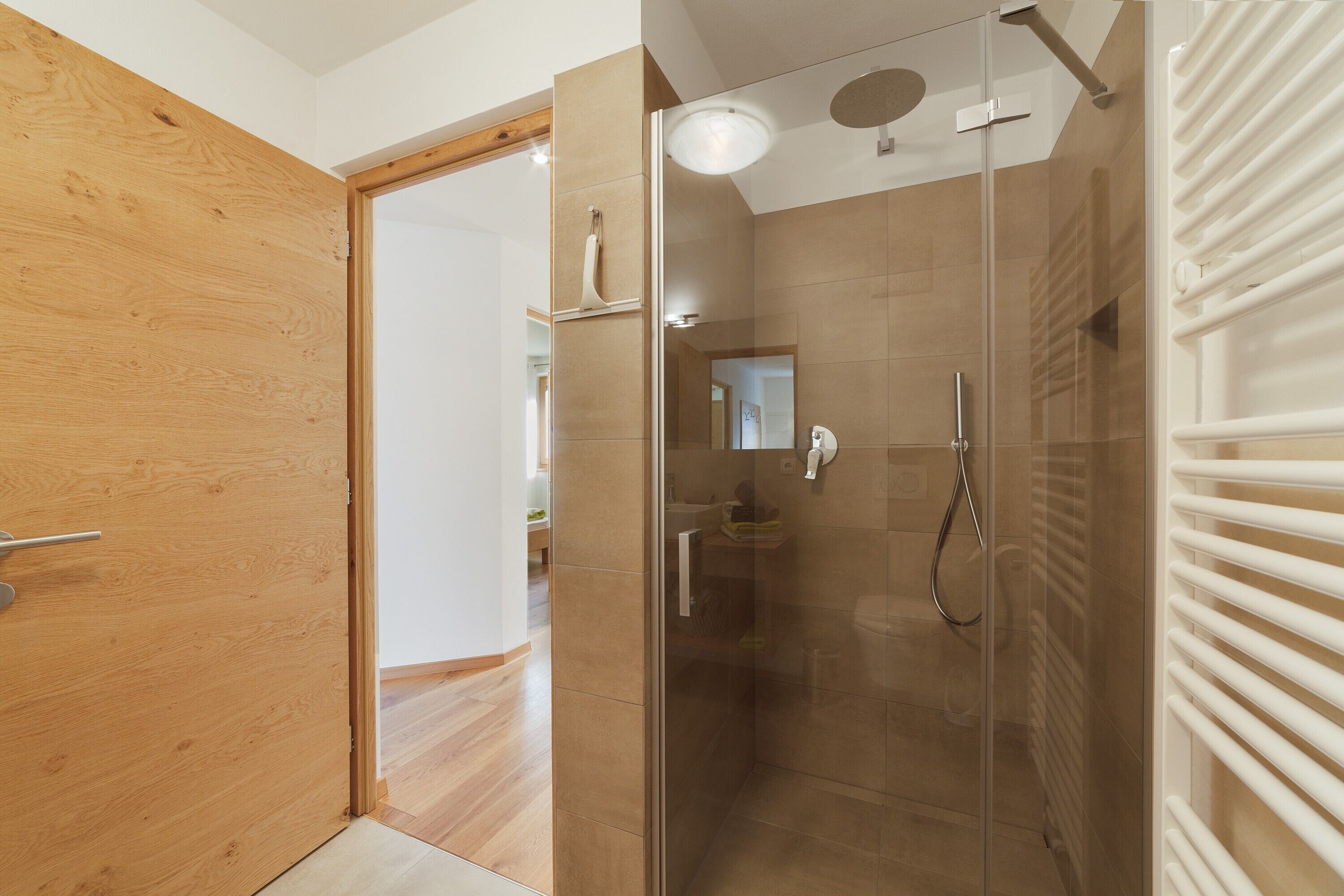 Une salle de bain moderne avec une douche à parois de verre, un porte-serviettes blanc et une porte en bois.