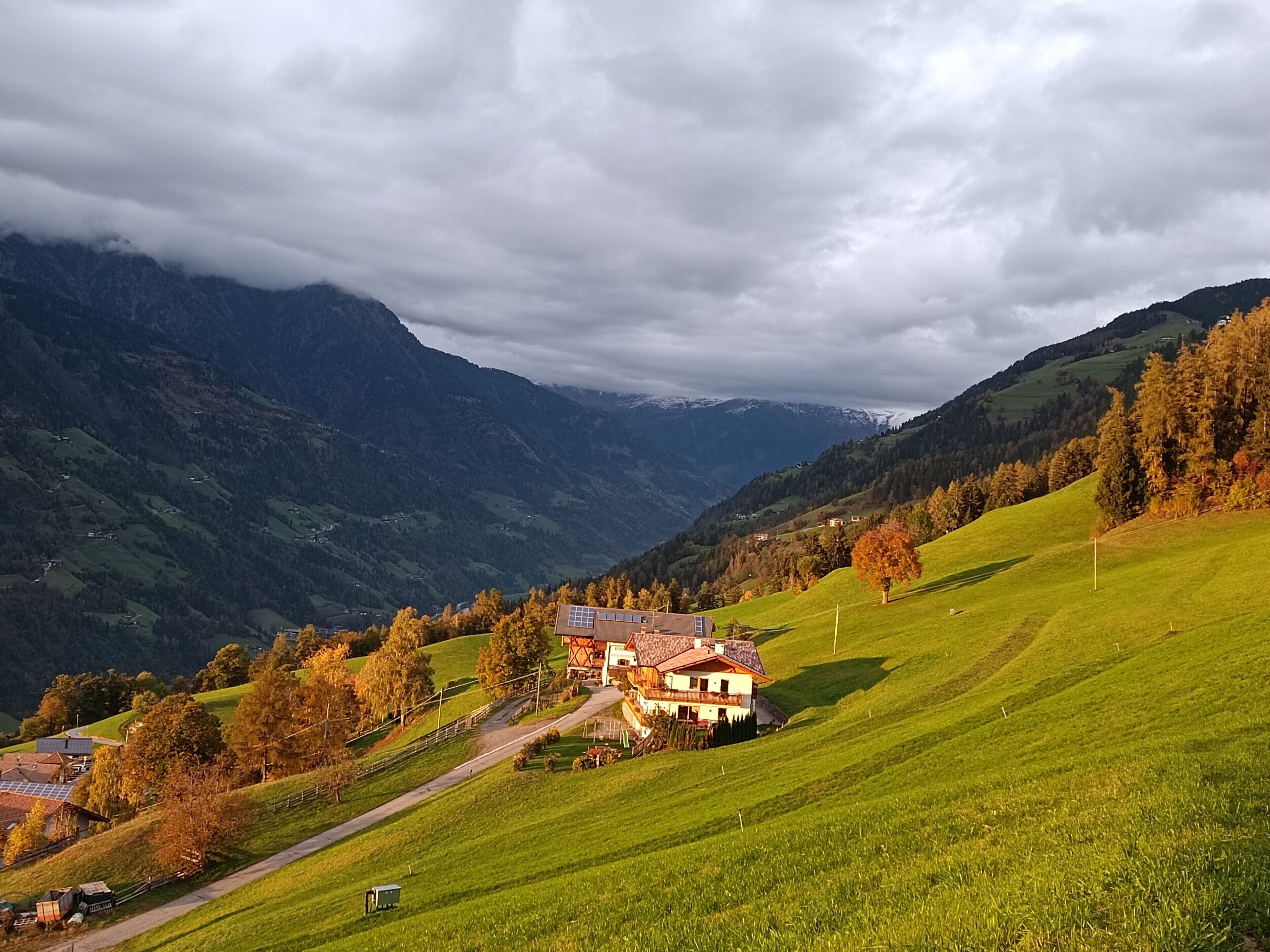 A house with a sloped roof, surrounded by a green landscape and mountains in the background.