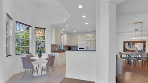 Een moderne keuken met witte kasten, een centraal eiland en een eetgedeelte met een ronde tafel en stoelen.