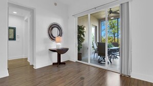 Een ruime kamer met een houten vloer, een eettafel met stoelen, een wandspiegel en een schuifdeur van glas die leidt naar een terras buiten met een tafel en stoelen.