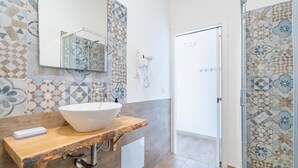 Un bagno con un lavandino bianco capiente, un piano d'appoggio in legno, uno specchio e piastrelle decorate sulle pareti.