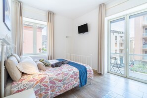 Et soveværelse med seng, fjernsyn og en balkon med udsigt til bygninger.