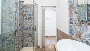 A bathroom with patterned tiles, a glass shower enclosure, a white bathtub, and a door leading to another room. - Guest House 'Raudino Rooms - Maniace' with Balcony, Wi-Fi and Air Conditioning (Siracusa)