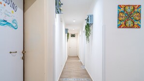 Un pasillo con piso de madera, paredes blancas y una obra de arte colorida a la derecha.