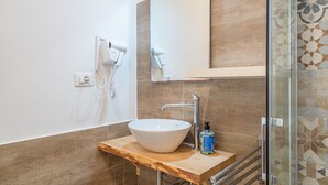 Un baño con lavamanos blanco, espejo, secador de pelo y zona de ducha.